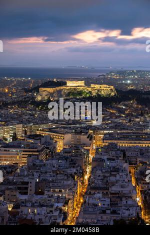 Blick über das Meer der Häuser von Athen, beleuchteter Parthenon-Tempel auf der Akropolis, dramatisch bewölkter Himmel bei Sonnenuntergang, vom Berg Lycabettus, Athen, Gr Stockfoto