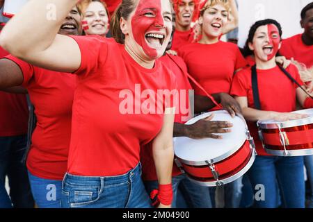 Multirassische rote Sportfans, die beim Unterstützen ihres Teams kreischen - Fußballfans, die Spaß bei Wettkampfveranstaltungen haben - konzentrieren sich auf das Gesicht einer älteren Frau Stockfoto