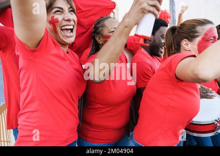 Multirassische rote Sportfans, die schreien, während sie ihr Team unterstützen – Fußballfans, die Spaß beim Wettkampf haben – Fokus auf afrikanisches Frauenohr Stockfoto