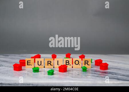 Word EURIBOR ist in Holzbuchstaben auf grauem Hintergrund geschrieben. Um Word kleine Häuser in Rot und Grün. Konzept der Verringerung von Einsparungen. Stockfoto