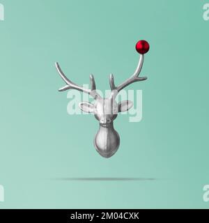 Weihnachtliches Rentierkonzept auf blauem Hintergrund mit Rentierkopf und roter Kugel. Minimaler Winterurlaub, Neujahrskonzept Stockfoto