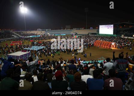 Doha, Katar. 03.. Dezember 2022. Arbeiter, hauptsächlich aus Indien, Bangladesch, Nepal und anderen ärmeren asiatischen Ländern, sehen das Spiel Argentinien-Australien auf einer großen Leinwand im Asian Town Cricket Stadium. Im Cricket-Stadion, das offiziell als „Fan Zone Industrial Area“ bezeichnet wird, sehen sich jeden Abend Tausende von ausländischen Arbeitern die Fußballspiele der Weltmeisterschaft an. Kredit: Christian Charisius/dpa/Alamy Live News Stockfoto