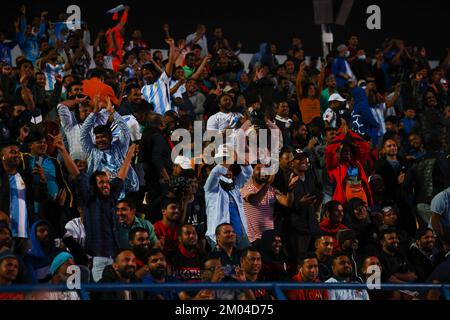 Doha, Katar. 03.. Dezember 2022. Arbeiter, hauptsächlich aus Indien, Bangladesch, Nepal und anderen ärmeren asiatischen Ländern, sehen das Spiel Argentinien-Australien auf einer großen Leinwand im Asian Town Cricket Stadium. Im Cricket-Stadion, das offiziell als „Fan Zone Industrial Area“ bezeichnet wird, sehen sich jeden Abend Tausende von ausländischen Arbeitern die Fußballspiele der Weltmeisterschaft an. Kredit: Christian Charisius/dpa/Alamy Live News Stockfoto