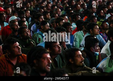 Doha, Katar. 03.. Dezember 2022. Arbeiter, hauptsächlich aus Indien, Bangladesch, Nepal und anderen ärmeren asiatischen Ländern, sehen das Spiel Argentinien-Australien auf einer großen Leinwand im Asian Town Cricket Stadium. Im Cricket-Stadion, das offiziell als „Fan Zone Industrial Area“ bezeichnet wird, sehen sich jeden Abend Tausende von ausländischen Arbeitern die Fußballspiele der Weltmeisterschaft an. Kredit: Christian Charisius/dpa/Alamy Live News Stockfoto