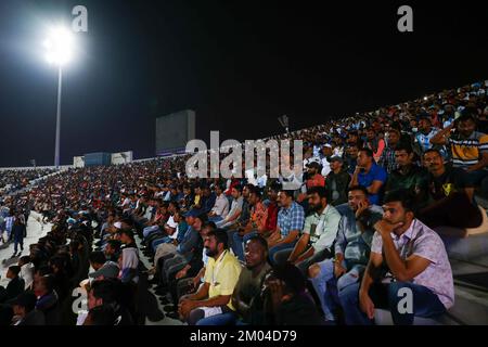 Doha, Katar. 03.. Dezember 2022. Arbeiter, hauptsächlich aus Indien, Bangladesch, Nepal und anderen ärmeren asiatischen Ländern, sehen das Spiel Argentinien-Australien auf einer großen Leinwand im Asian Town Cricket Stadium. Im Cricket-Stadion, das offiziell als „Fan Zone Industrial Area“ bezeichnet wird, sehen sich jeden Abend Tausende von ausländischen Arbeitern die Fußballspiele der Weltmeisterschaft an. Kredit: Christian Charisius/dpa/Alamy Live News Stockfoto