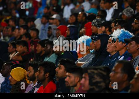 Doha, Katar. 03.. Dezember 2022. Arbeiter, hauptsächlich aus Indien, Bangladesch, Nepal und anderen ärmeren asiatischen Ländern, sehen das Spiel Argentinien-Australien auf einer großen Leinwand im Asian Town Cricket Stadium. Im Cricket-Stadion, das offiziell als „Fan Zone Industrial Area“ bezeichnet wird, sehen sich jeden Abend Tausende von ausländischen Arbeitern die Fußballspiele der Weltmeisterschaft an. Kredit: Christian Charisius/dpa/Alamy Live News Stockfoto