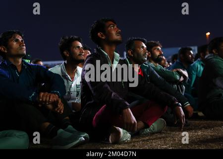 Doha, Katar. 03.. Dezember 2022. Arbeiter, hauptsächlich aus Indien, Bangladesch, Nepal und anderen ärmeren asiatischen Ländern, sehen das Spiel Argentinien-Australien auf einer großen Leinwand im Asian Town Cricket Stadium. Im Cricket-Stadion, das offiziell als „Fan Zone Industrial Area“ bezeichnet wird, sehen sich jeden Abend Tausende von ausländischen Arbeitern die Fußballspiele der Weltmeisterschaft an. Kredit: Christian Charisius/dpa/Alamy Live News Stockfoto