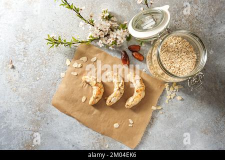 Gesunde Kekse, hausgemachte Mandelmondsiche ohne Zucker, aber mit Haferflocken und Datteln auf Backpapier, Zutaten und einem Frühlingsblumenzweig auf Rost Stockfoto