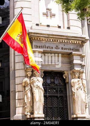 Madrid, Spanien - 20. Juni 2022: Spanische Flagge im Vordergrund und Eingang des Madrider Hauptquartiers des Cervantes-instituts, eines instituto, das di Stockfoto