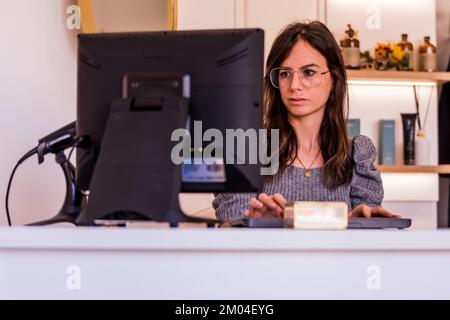 Junge Geschäftsfrau, Brünette mit Brille, arbeitet vor ihrem Computerbildschirm Stockfoto