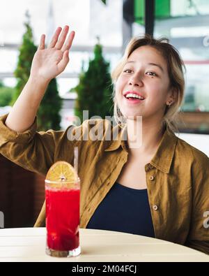 Wunderschönes asiatisches Mädchen, das Freunden die Hand winkt Stockfoto