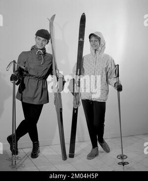 Winterkleidung in den 1950er. Ein junger Mann und eine junge Frau tragen die typischen Wintersportkleidung der 1950er Jahre. Tragen Sie eine praktische Windjacke, eine Skihose und ein Paar Skier und Stöcke. Schweden 1959. Conard Ref. 3933 Stockfoto