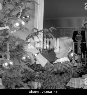 Weihnachten in den 1960er. Ein junges Mädchen steht am weihnachtsbaum und schmückt ihn. Schweden 1963 Ref. 4827 Stockfoto