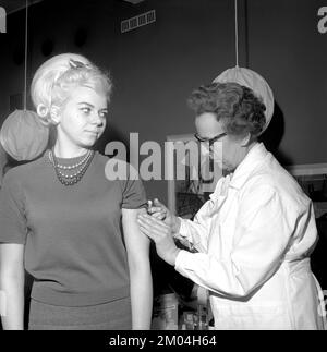 Impfstoff in den 1960er Jahren. Eine Krankenschwester injiziert einer jungen Frau einen Impfstoff in den Arm. Schweden 1965 Conard Ref 5011 Stockfoto