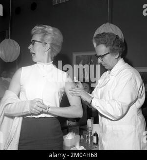 Impfstoff in den 1960er Jahren. Eine Krankenschwester injiziert einen Impfstoff in den Arm einer jungen Frau, die ihn nicht zu mögen scheint. Schweden 1965 Conard Ref 5011 Stockfoto