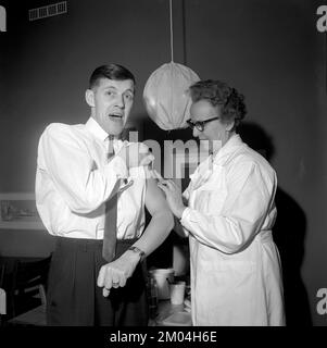 Impfstoff in den 1960er Jahren. Eine Krankenschwester injiziert einem Mann einen Impfstoff in den Arm. Es sieht so aus, als würde es ihm nicht gefallen. Schweden 1965 Conard Ref 5011 Stockfoto