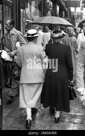 Regenschirme in den 1950er Jahren. Der Regen strömt in Strömen und zwei ältere Damen halten sich beim Gehen mit dem Schirm über den Kopf. Es ist ein Regentag in Stockholm Schweden 1953. ref. 1,2 Stockfoto