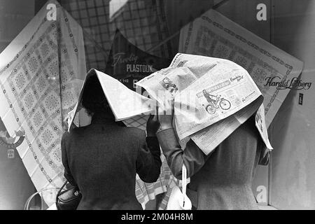 Regenschirme in den 1950er Jahren. Der Regen strömt in Strömen und zwei Damen halten die Tageszeitungen über sich, da sie keinen Schirm haben. Es ist ein Regentag in Stockholm Schweden 1953. ref. 1,2 Stockfoto