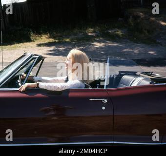 In den 1960er Jahren. Eine blonde junge Frau auf dem Fahrersitz eines Cabrios. Schweden 1960er Stockfoto