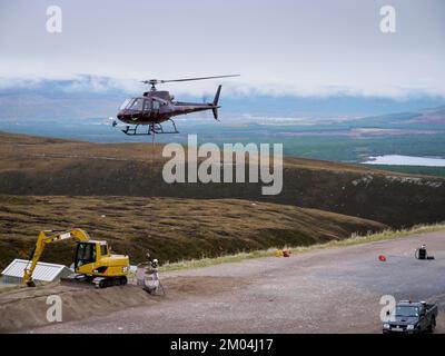 Aviemore, Schottland, Großbritannien. Aufgenommen am 14. Oktober 2009. Der Hubschrauber hebt Steinsäcke in die Luft. Ein Mann, der ein Seil an Tonnen Steinsäcken befestigt. Stockfoto