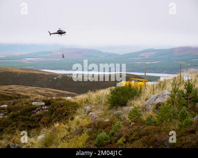 Aviemore, Schottland, Großbritannien. Aufgenommen am 14. Oktober 2009. Der Hubschrauber hebt Steinsäcke in die Luft. Ein Mann, der ein Seil an Tonnen Steinsäcken befestigt. Stockfoto