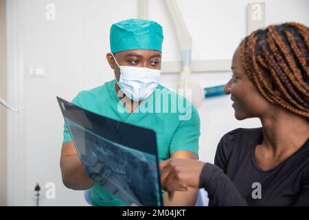 Ein Zahnarzt zeigt seinem Patienten Röntgenbilder, afrikanische Zahnklinik Stockfoto