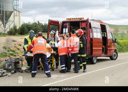 Feuerwehrauto mit Feuerwehrleuten, Sanitätern und Zivilwachen, die bei einem Verkehrsunfall eine verletzte Person behandeln und ermutigen. Stockfoto