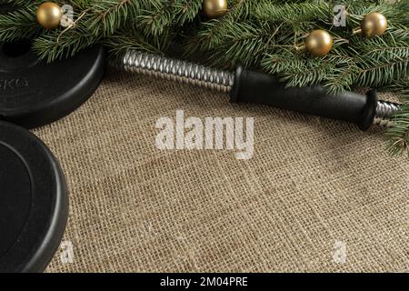Hantelglockengewichtsteller, Weihnachtsbaumzweige, Dekorationen. Fitness-Feiertage Winterzusammensetzung. Fitnesskonzept mit Kopierbereich. Stockfoto