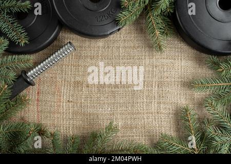 Kurzhanteln, Gewichtsteller und Weihnachtsbaumzweige. Fitness-Feiertage Winterzusammensetzung. Fitnessstudio Training flach liegendes Design mit Kopierbereich. Stockfoto