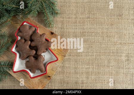 Schokoladen-Lebkuchen-Mann, Weihnachtskekse und Baumzweige. Weihnachtszeit Winterkomposition mit Kopierbereich auf Jutematerial. Stockfoto