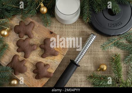 Schokoladen-Lebkuchen-Weihnachtskekse, Kurzhanteln-Gewichtsteller, ein Glas Milch für den Weihnachtsmann. Fitness, Winterdiät, Fitnessstudio, Diätkonzept. Stockfoto