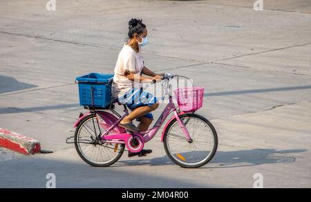 SAMUT PRAKAN, THAILAND, 02 2022. MÄRZ, Eine Frau fährt auf einem Fahrrad mit Körben zum Laden auf einer Stadtstraße. Stockfoto