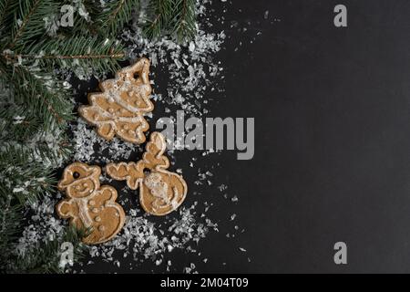 Lebkuchen-Weihnachtskekse mit Glasur oder Zuckerguss und Äste. Weihnachtszeit Winterkomposition mit Kopierbereich auf schwarzem Hintergrund. Stockfoto