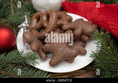 Schokoladen-Lebkuchen-Weihnachtskekse auf einem weißen Teller. Mit Weihnachtsmannmütze, Ästen und roten Schmucksteinen. Stockfoto