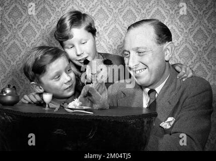 Foto von Harry Corbett mit Sooty and Sons David, 9 auf der linken Seite, und Peter (besser bekannt als Matthew Corbett), 6 Jahre alt. Datum: 8/2/1955. Ruoty wird 2023 75 Jahre im Showbusiness feiern, wobei der aktuelle Wächter des unverwechselbaren Gelbbbären sagt, Einfachheit sei der Schlüssel zu seiner dauerhaften Beliebtheit. Sidekicks Sweep, Soo und Richard Cadell werden im nächsten Jahr zusammen mit Ruoty eine Theatertour und eine neue Fernsehserie machen, aber davor gibt es eine Stint in Pantomime und eine weitere Promotion für eine WeihnachtsSingle, die Geld für die Wohltätigkeitsorganisation Childline sammelt. Ausgabedatum: 8. Februar 1955. Stockfoto