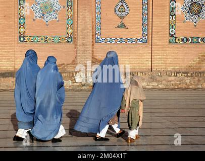 Herat im Westen Afghanistans. Die große Moschee von Herat (Freitagsmoschee oder Jama Masjid). Drei Frauen in Burka und ein Mädchen gehen vor die Moschee. Stockfoto