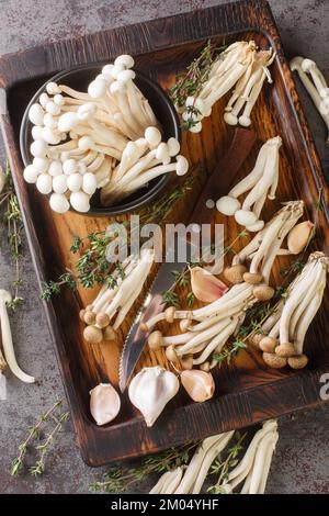 Frische weiße und braune Shimeji essbare oder Buche Pilze mit Kochzutaten auf Holzbrett auf dem Tisch. Vertikale Draufsicht von oben Stockfoto