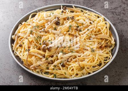 Spaghetti-Pasta mit gebratenen Shimeji-Buchenpilzen mit Parmesan und Thymian in Nahaufnahme auf einem Teller auf dem Tisch. Horizontal Stockfoto