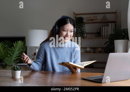 Lächelndes Mädchen Student tragen Kopfhörer Studie online mit Lehrer, glücklich junge asiatische Frau lernen Sprache hören Vortrag sehen Webinar schreiben Notizen ansehen Stockfoto