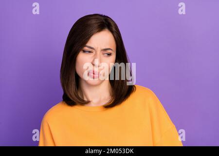 Nahaufnahme Foto einer jungen hübschen, hübschen, netten, Mädchenfrau tragen orangefarbenen Pullover gegossene Lippen unglücklich aussehen leerer Raum unzufrieden isoliert auf violetter Farbe Stockfoto