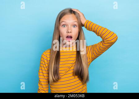 Foto eines überraschten, beeindruckenden Schulmädchens mit gestreiften langen Ärmeln Hand am Kopf halten, isoliert auf blauem Hintergrund Stockfoto