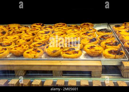 Tablett mit Pastel de Nata hinter einem Fenster. Ein Pastel de nata, wörtlich „Cream Gebäck“, ist ein typisch portugiesisches Gebäck. Es ist eine Art Gebäck Stockfoto