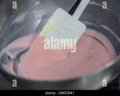 Der Konditorchef füllt den Rührbeutel mit essbarer rosafarbener Farbe für die Farbskala und die Aufnahme von Kuchenfilmen Stockfoto