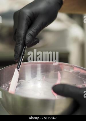 Der Konditorchef füllt den Rührbeutel mit essbarer rosafarbener Farbe für die Farbskala und die Aufnahme von Kuchenfilmen Stockfoto