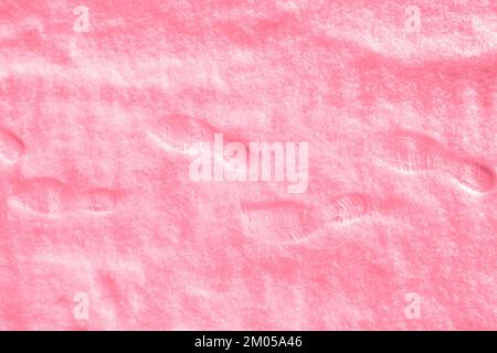 Mehrere menschliche Fußspuren in Schuhen auf frisch gefallenem Schnee. Winter schneereich Hintergrund. Draufsicht. Trendige Farbtöne 2023 Viva Magenta. Stockfoto