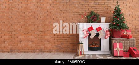 Kamin mit Weihnachtssocken, Kranz, Tanne und Geschenken in der Nähe von Ziegelwänden im Zimmer Stockfoto