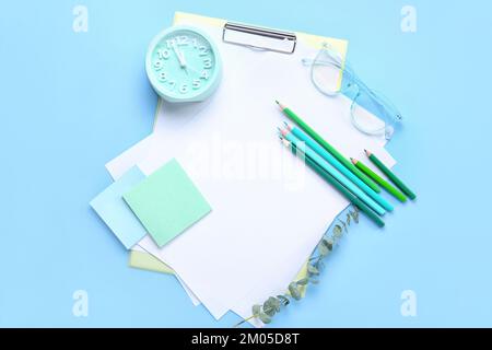 Klemmbrett mit leeren Papierblättern, Bleistiften, Wecker, Haftnotizen und Brille auf blauem Hintergrund Stockfoto