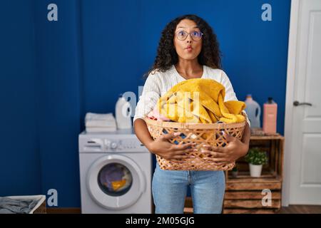 Eine junge hispanikerin, die Wäsche wäscht und einen Korb hält. Sie macht Fischgesicht mit Mund und schielenden Augen, verrückt und komisch. Stockfoto