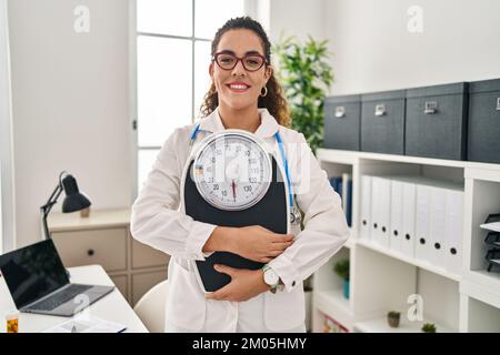 Junge hispanische Frau, die in einer Diätistischen Klinik arbeitet und mit einem fröhlichen und kühlen Lächeln im Gesicht lächelt. Zähne zeigen. Stockfoto