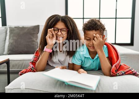 Zwei Geschwister, die auf dem Sofa lagen und ein Buch mit Fingergesten lesen, lächelten mit Hoffnung und geschlossenen Augen. Glück und abergläubisches Konzept. Stockfoto